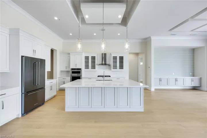 Kitchen with stainless steel appliances, white cabinetry, decorative light fixtures, a kitchen island with sink, and glass insert cabinets