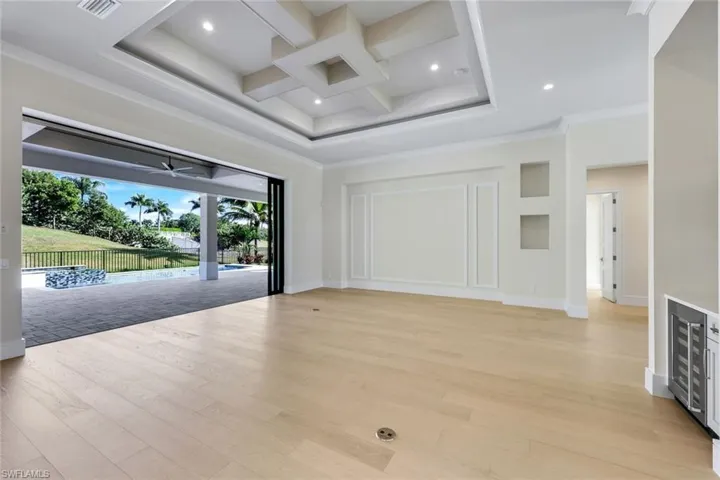 Empty room with coffered ceiling, beam ceiling, beverage cooler, light wood-type flooring, and ornamental molding