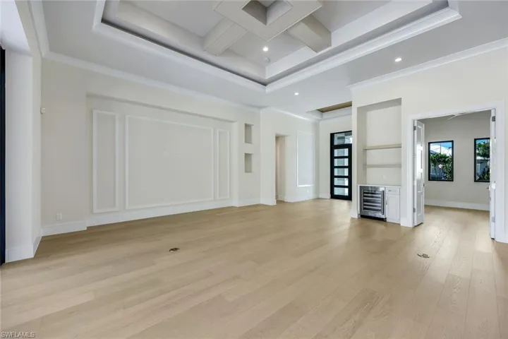 Unfurnished living room featuring coffered ceiling, beamed ceiling, light wood-type flooring, wine cooler, and crown molding