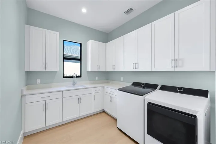 Laundry room featuring separate washer and dryer, light wood-style flooring, cabinet space, and recessed lighting