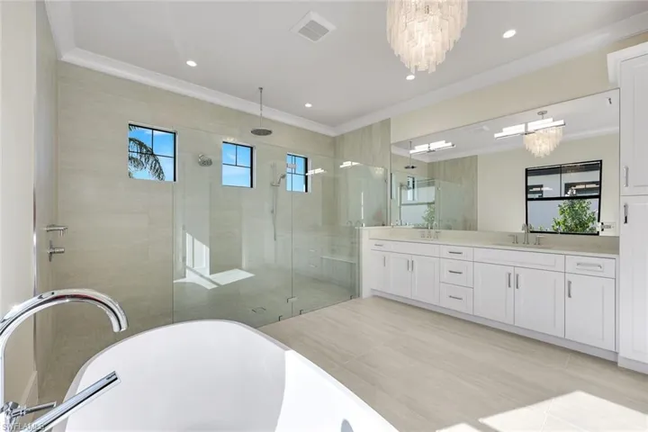 Bathroom featuring double vanity, a soaking tub, a stall shower, a chandelier, and ornamental molding