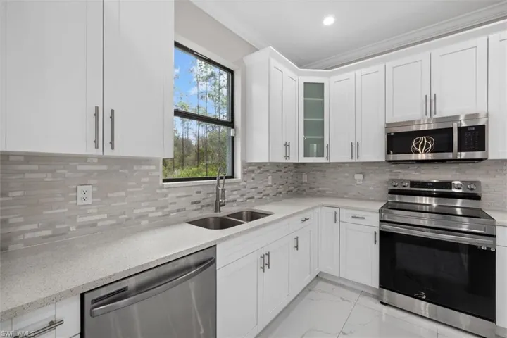 Kitchen featuring a sink, ornamental molding, appliances with stainless steel finishes, decorative backsplash, and marble finish floor