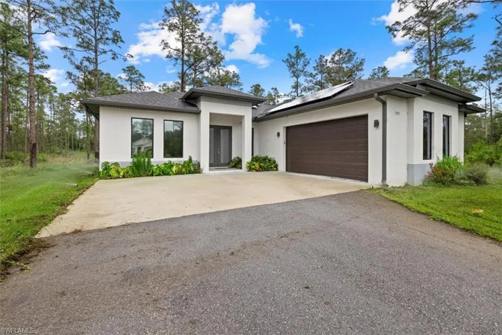 Modern Style house with roof mounted solar panels, stucco siding, an attached garage, a shingled roof, and driveway