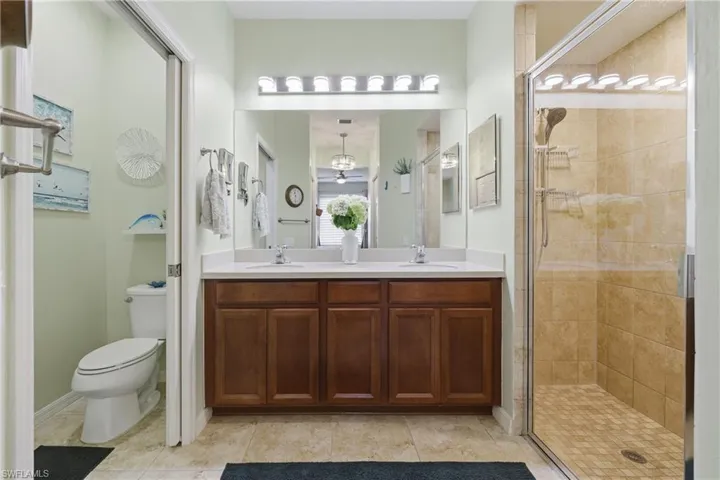 Primary bath featuring a tiled shower stall, double vanity, new light fixture and light tile patterned floors