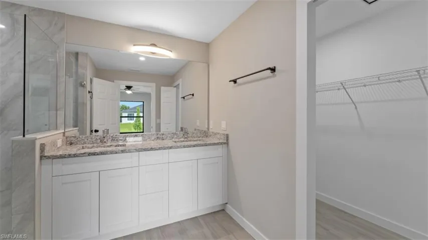 Full bathroom featuring a walk in closet, double vanity, a sink, baseboards, and walk in shower