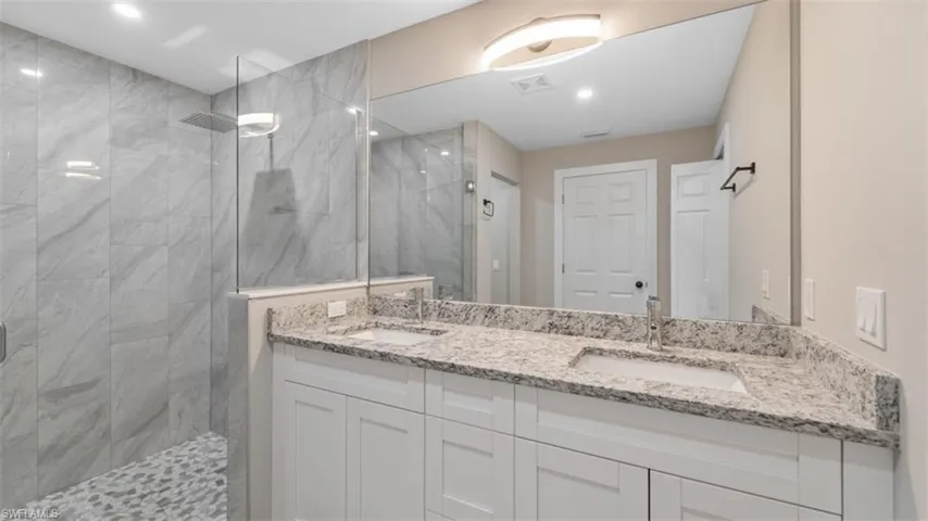 Full bathroom featuring a tile shower, double vanity, a sink, and visible vents
