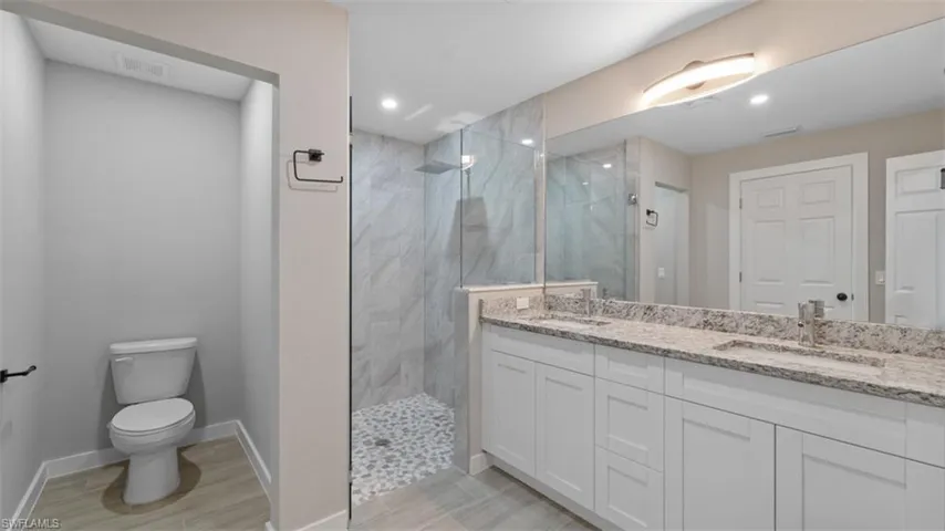 Bathroom featuring toilet, a sink, a marble finish shower, and double vanity