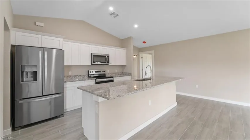 Kitchen with appliances with stainless steel finishes, white cabinets, a sink, and an island with sink