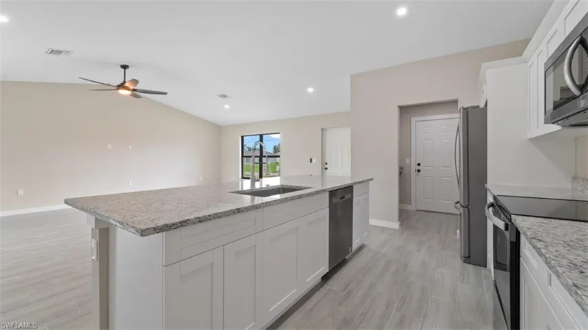 Kitchen featuring appliances with stainless steel finishes, white cabinetry, a sink, and a center island with sink