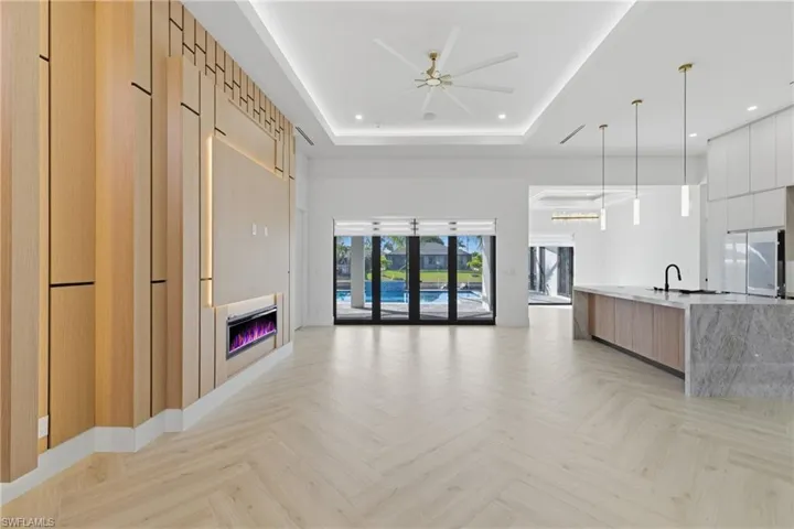 Unfurnished living room featuring parquet flooring, a raised ceiling, ceiling fan, and suspended lighting