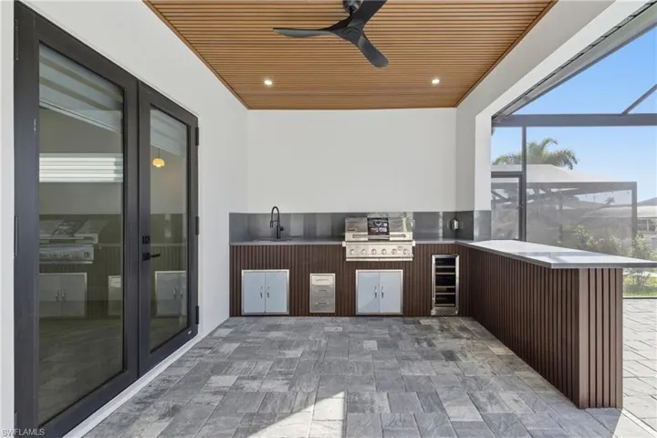 View of patio featuring glass enclosure, exterior kitchen, a sunroom, a ceiling fan, and wine cooler