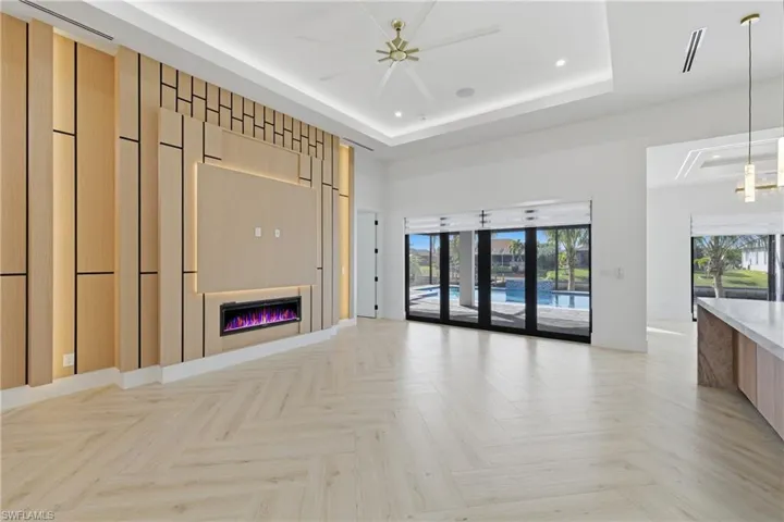 Unfurnished living room with a glass covered fireplace, parquet flooring, and a tray ceiling