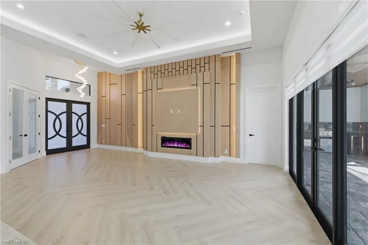 Unfurnished living room with parquet floors, french doors, a raised ceiling, a glass covered fireplace, and recessed lighting