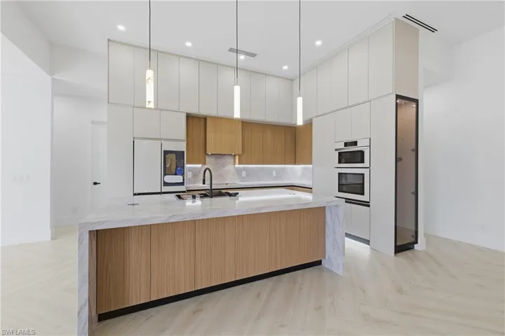 Two tone kitchen with parquet flooring, light stone counters, modern cabinets, decorative light fixtures, and a high ceiling