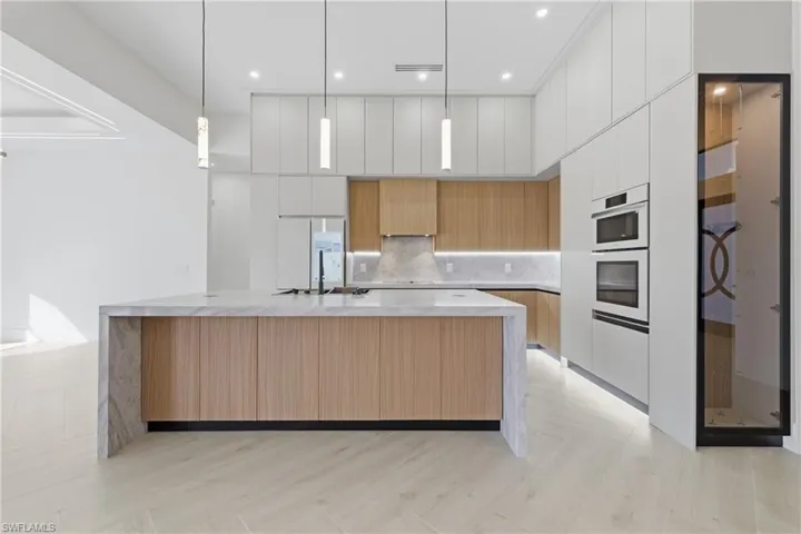 Kitchen with modern cabinets, pendant lighting, two tone color scheme, a spacious island, and light stone counters