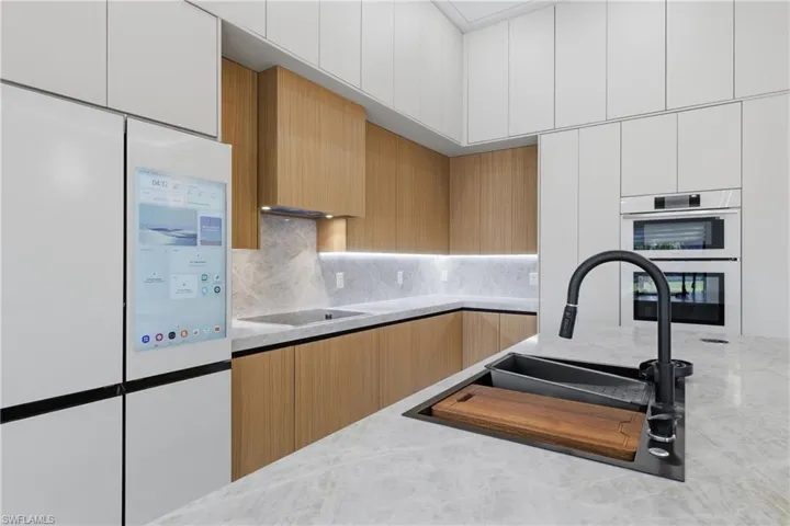 Kitchen with white appliances, modern cabinets, decorative backsplash, light stone counters, and dual tone cabinets