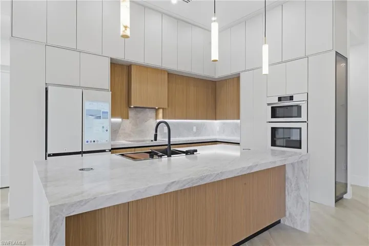 Kitchen with light stone countertops, modern cabinets, white appliances, an island with sink, and two tone cabinetry