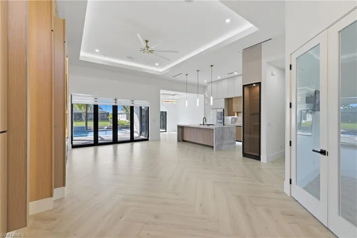 Unfurnished living room with french doors, parquet floors, a ceiling fan, a tray ceiling, and recessed lighting
