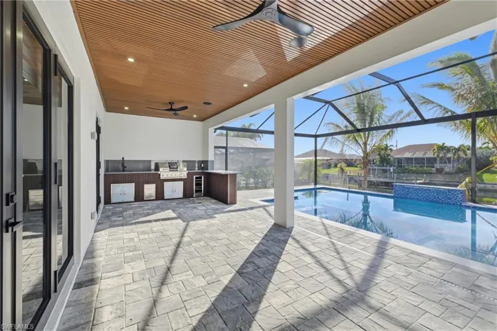Outdoor pool featuring exterior kitchen, a sunroom, a patio, and glass enclosure