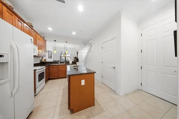 Kitchen featuring white appliances, ornamental molding, wood finish cabinetry, light tile patterned floors, and dark stone countertops