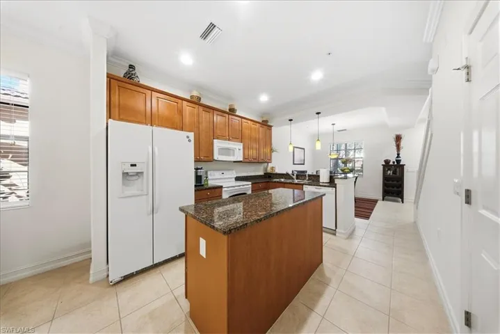 Kitchen featuring wood finish cabinetry, white appliances, dark stone countertops, a center island, and pendant lighting