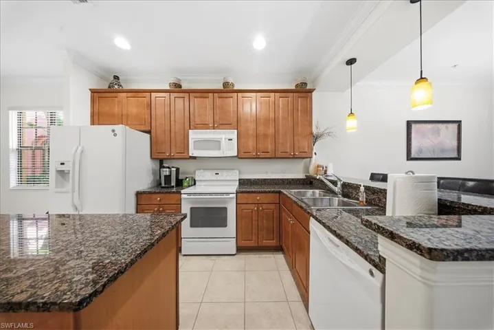 Kitchen with wood finish cabinets, dark stone counters, white appliances, crown molding, and pendant lighting