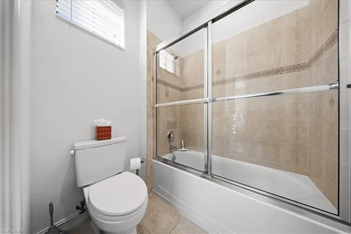 Bathroom with bath / shower combo with glass door and light tile patterned flooring