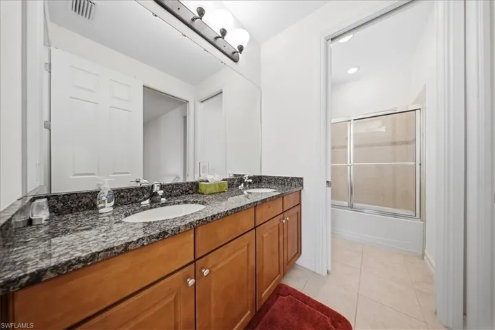 Bathroom with shower / bath combination with glass door, double vanity, and light tile patterned floors