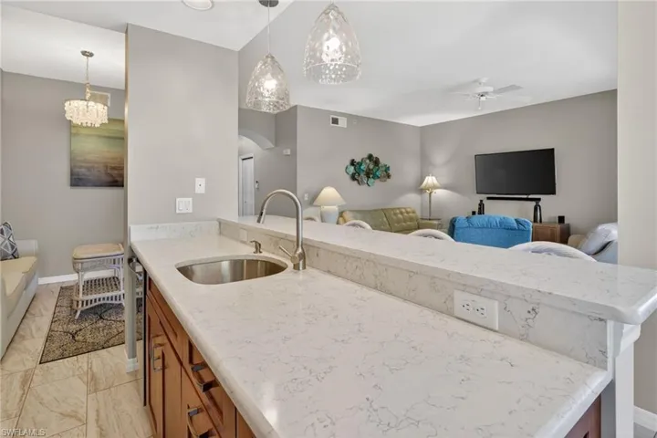 Kitchenette featuring a stainless steel sink, a gooseneck faucet, and light-toned countertops with a subtle vein pattern