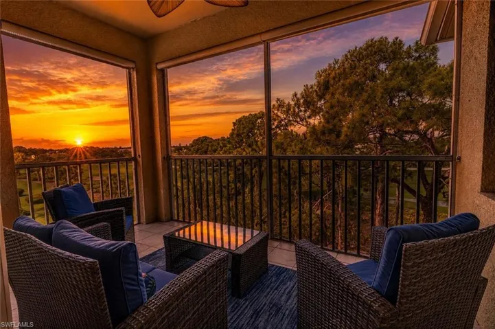 Screened balcony featuring a tiled floor, dark railing, and a scenic sunset backdrop over distant trees and a golf course