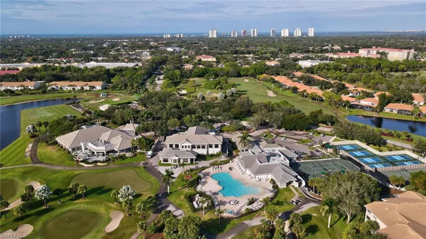 Expansive aerial perspective showcasing a golf course, multiple buildings with light-toned roofs, a large outdoor swimming pool, and several tennis courts