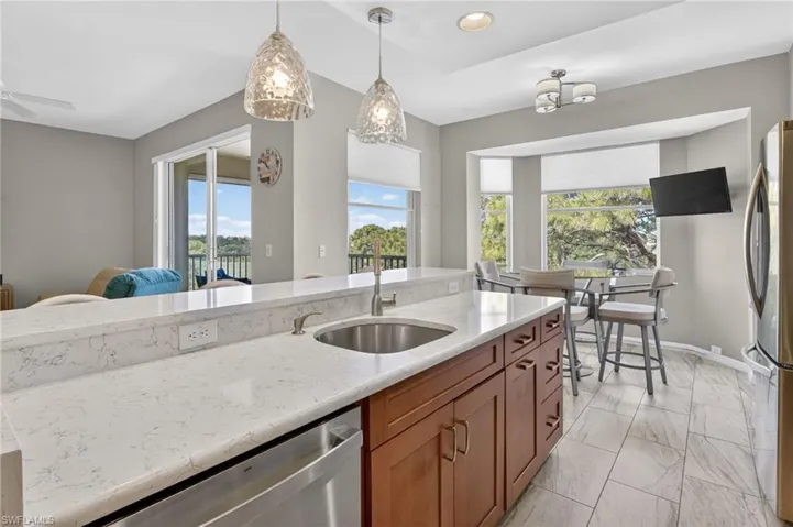 Kitchen featuring an island with white stone countertops, a stainless steel sink, and a built-in dishwasher