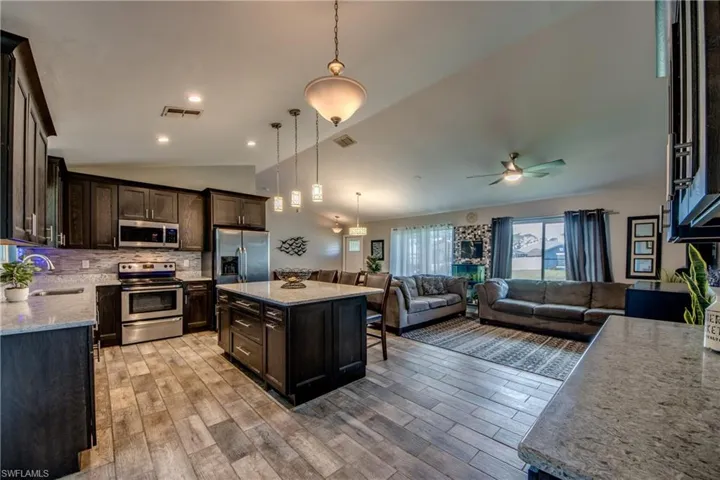 Kitchen featuring dark brown cabinets, pendant lighting, backsplash, a center island, and appliances with stainless steel finishes