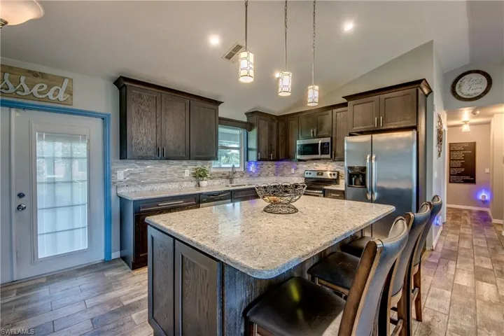 Kitchen with stainless steel appliances, pendant lighting, a kitchen island, backsplash, and lofted ceiling