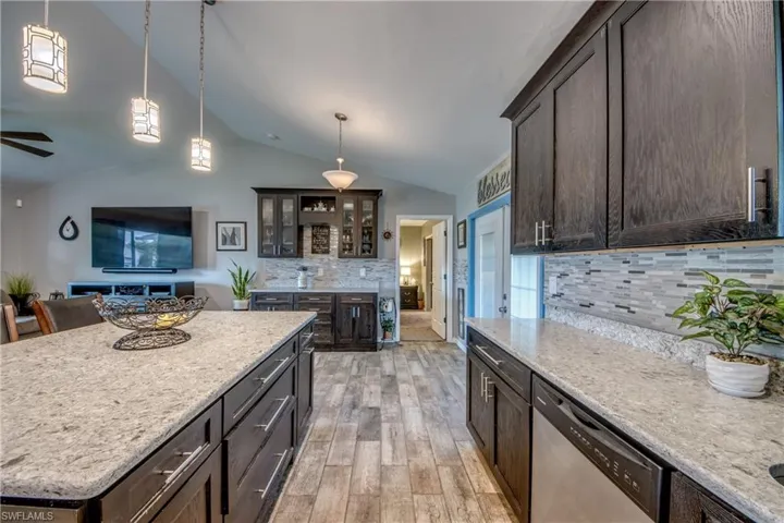 Kitchen with backsplash, ceiling fan, stainless steel dishwasher, light wood-type flooring, and lofted ceiling