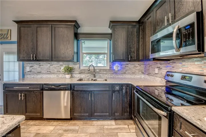 Kitchen with backsplash, appliances with stainless steel finishes, sink, and light stone counters