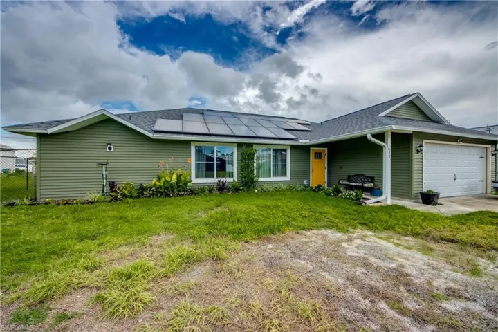 Single story home featuring a garage, a front lawn, and solar panels