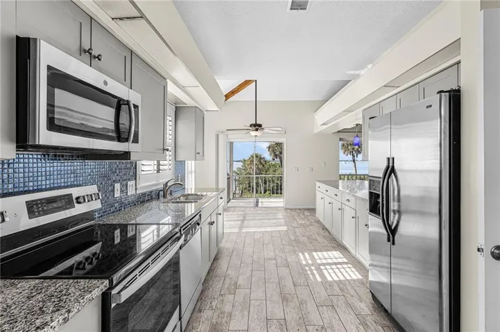 Kitchen featuring stainless steel appliances, light stone countertops, wood finish floors, decorative backsplash, and a textured ceiling