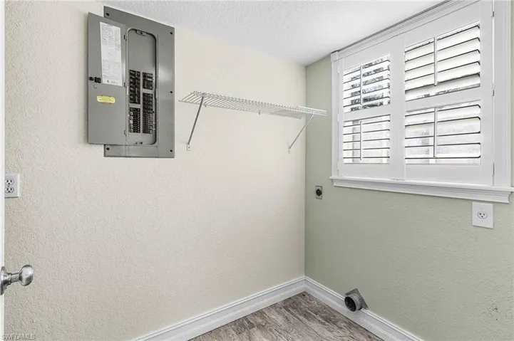 Laundry room with electric panel, a textured wall, a textured ceiling, light wood finished floors, and electric dryer hookup