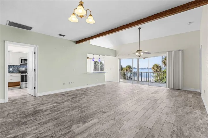 Unfurnished living room featuring a water view, wood tiled floors, a ceiling fan, suspended lighting, and lofted ceiling with beams