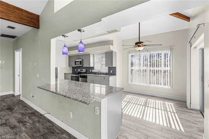 Kitchen featuring beam ceiling, gray cabinets, light stone counters, light wood-style floors, and a peninsula