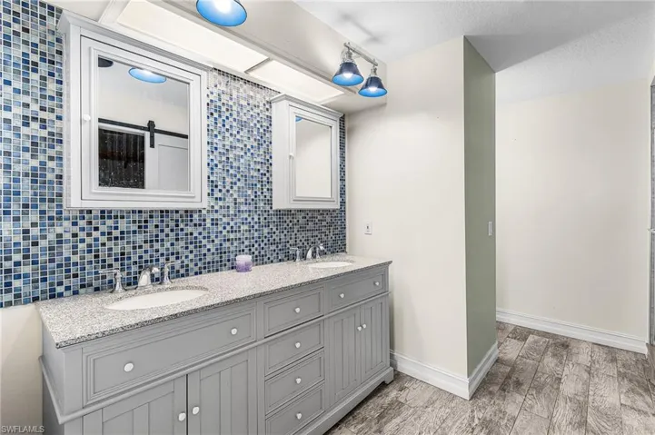 Bathroom with double vanity, backsplash, and light wood-style floors