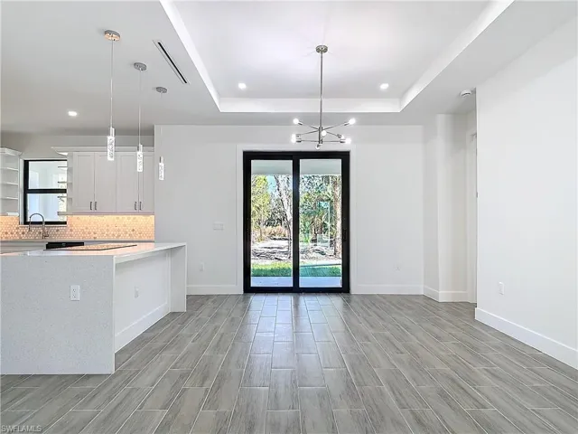 Kitchen featuring open floor plan, a tray ceiling, light countertops, white cabinetry, and backsplash