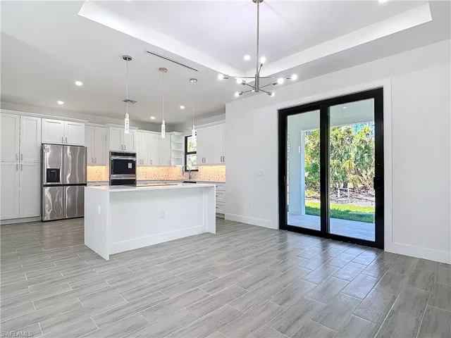 Kitchen featuring white cabinets, stainless steel fridge with ice dispenser, light countertops, backsplash, and a center island