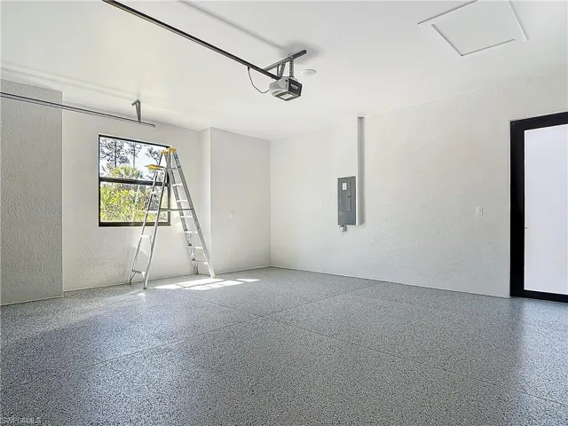 Garage with a textured wall, electric panel, and a garage door opener