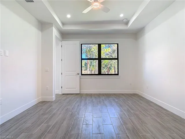 Unfurnished room with a tray ceiling, wood finish floors, recessed lighting, a ceiling fan, and baseboards
