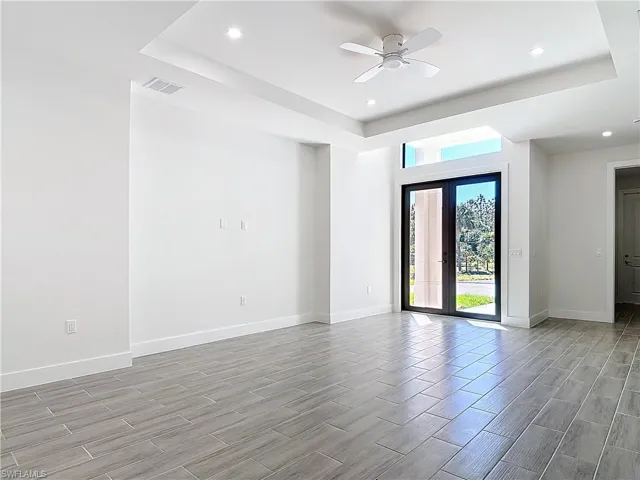 Unfurnished room with wood finish floors, a ceiling fan, visible vents, baseboards, and a raised ceiling