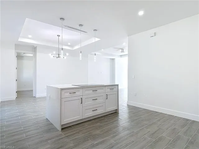 Kitchen featuring black electric cooktop, a center island, hanging light fixtures, wood tiled floor, and a tray ceiling
