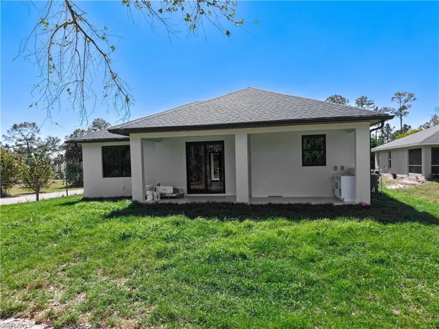Rear view of property featuring roof with shingles, a lawn, and stucco siding