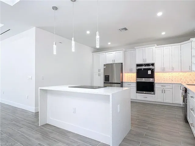 Kitchen with stainless steel appliances, a kitchen island, backsplash, and white cabinetry